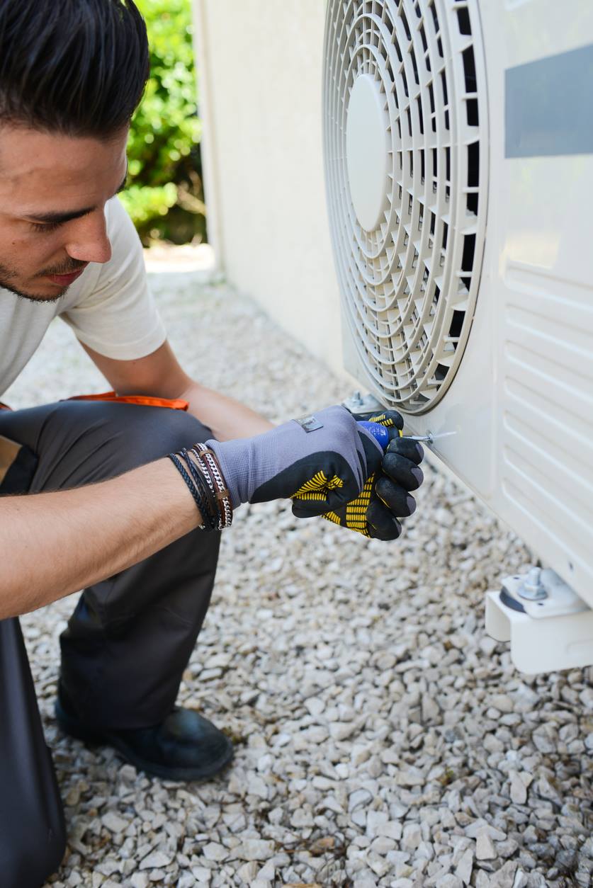 Technician testing components on a heat pump outdoor unit during a repair visit